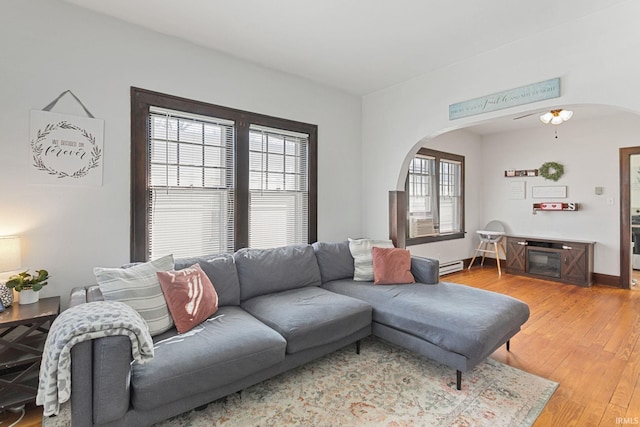 living area with arched walkways, baseboards, light wood finished floors, and a baseboard radiator