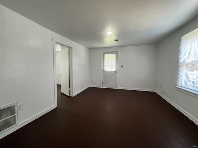 empty room with dark wood-style floors, a healthy amount of sunlight, visible vents, and baseboards