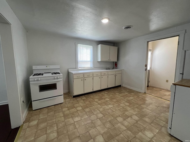 kitchen with white range with gas cooktop, visible vents, white cabinets, baseboards, and light countertops