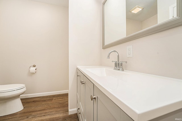 half bathroom with toilet, baseboards, wood finished floors, and vanity