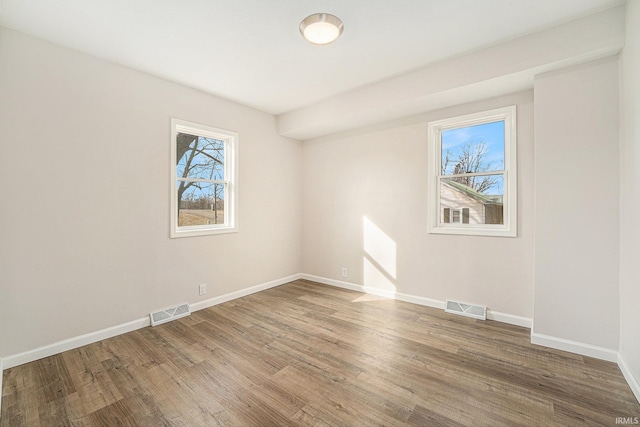 empty room featuring wood finished floors, visible vents, and baseboards