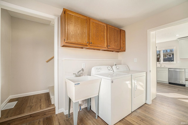 washroom featuring cabinet space, baseboards, washing machine and clothes dryer, light wood-type flooring, and a sink