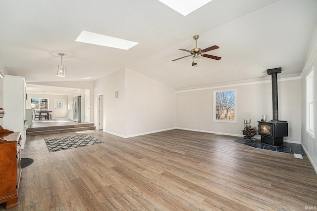 living area with a wealth of natural light, lofted ceiling with skylight, wood finished floors, and a wood stove