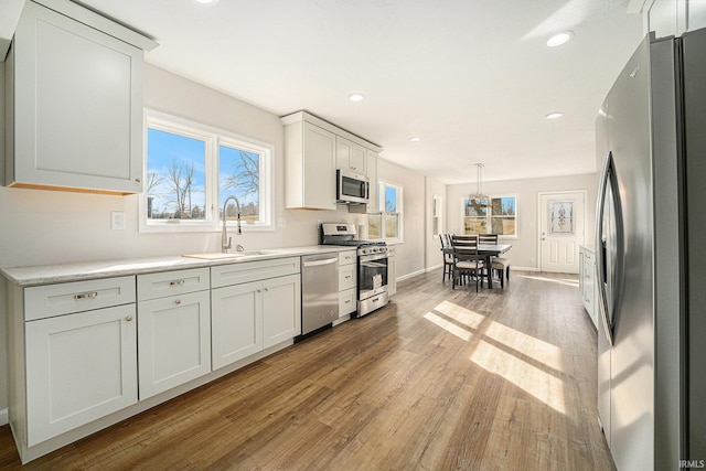 kitchen with appliances with stainless steel finishes, light countertops, a sink, and light wood-style flooring