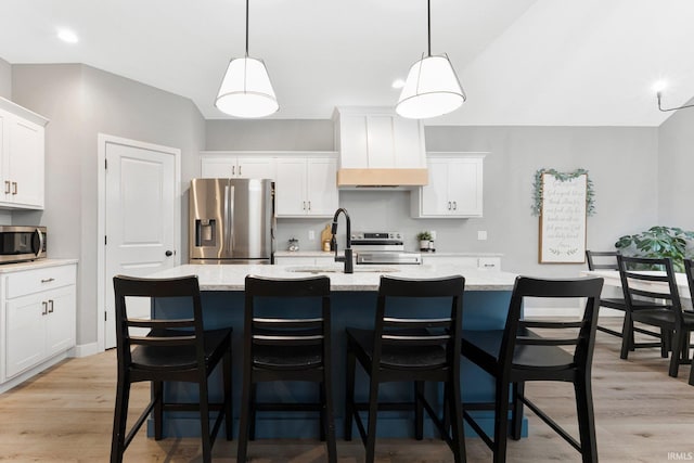 kitchen featuring stainless steel appliances, a center island with sink, white cabinets, and light wood-style floors