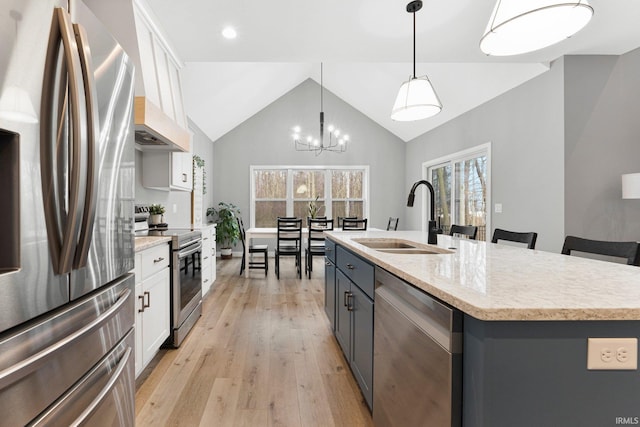 kitchen with light wood finished floors, stainless steel appliances, lofted ceiling, white cabinets, and a sink