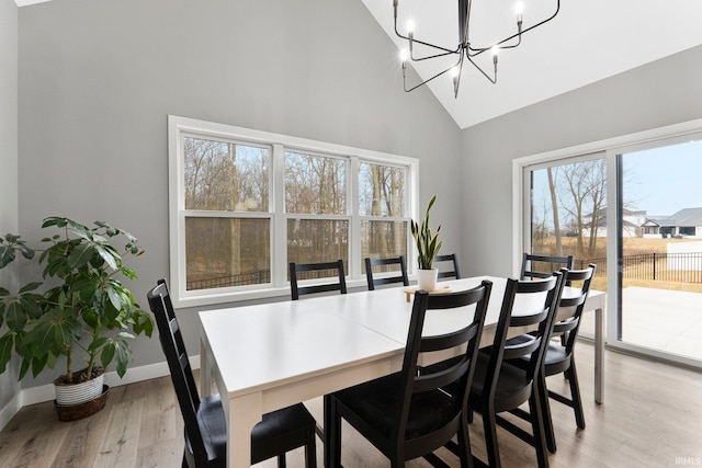 dining space featuring high vaulted ceiling, light wood finished floors, an inviting chandelier, and baseboards