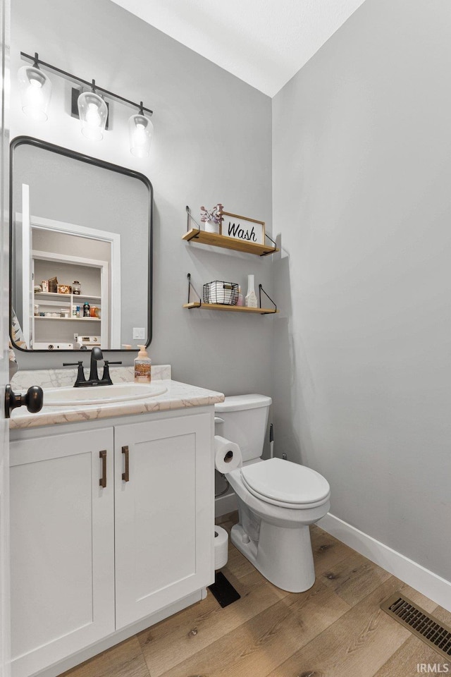 bathroom with visible vents, toilet, vanity, wood finished floors, and baseboards