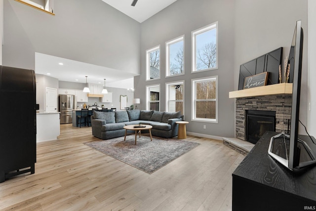 living room with a stone fireplace, light wood finished floors, recessed lighting, and baseboards