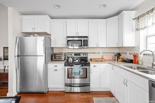 kitchen with white cabinetry, appliances with stainless steel finishes, a sink, and wood finished floors