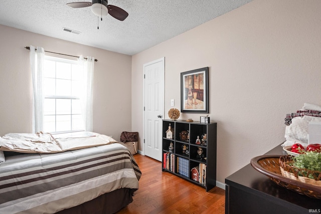 bedroom with a textured ceiling, wood finished floors, visible vents, baseboards, and a ceiling fan