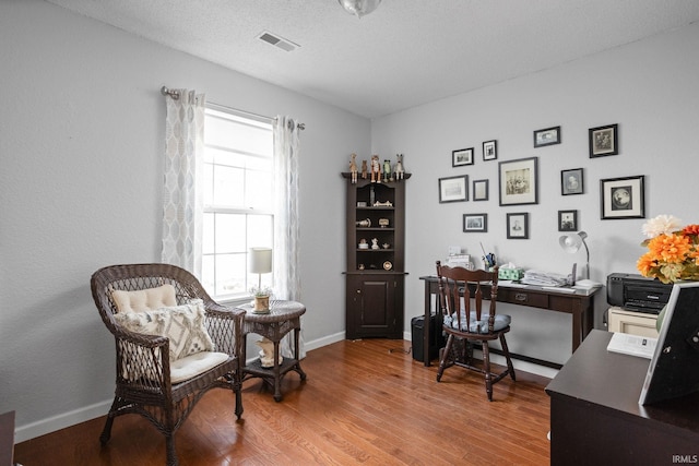 office space with baseboards, a textured ceiling, visible vents, and wood finished floors