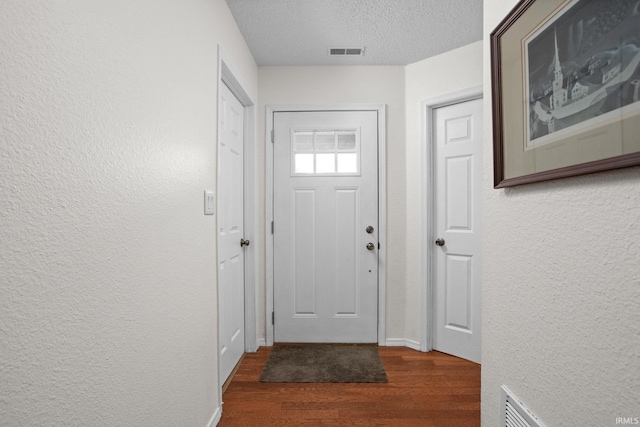 doorway to outside with a textured ceiling, a textured wall, wood finished floors, and visible vents