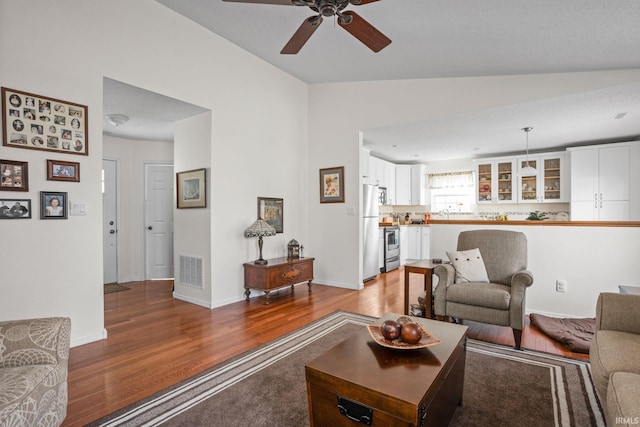 living area featuring vaulted ceiling, light wood-type flooring, visible vents, and baseboards