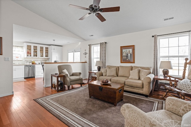 living area with wood-type flooring, visible vents, vaulted ceiling, and a ceiling fan