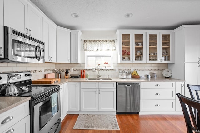 kitchen featuring white cabinets, appliances with stainless steel finishes, light countertops, light wood-type flooring, and a sink