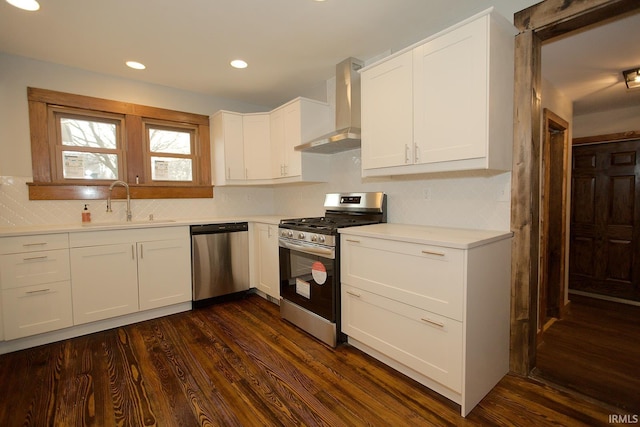 kitchen featuring wall chimney exhaust hood, appliances with stainless steel finishes, dark wood-style flooring, light countertops, and a sink