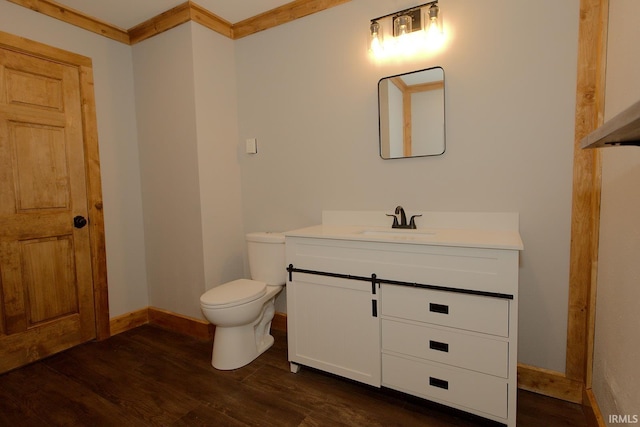 bathroom featuring toilet, wood finished floors, vanity, baseboards, and crown molding