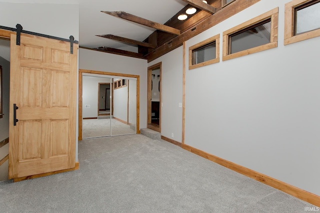 carpeted empty room with beam ceiling, baseboards, and a barn door