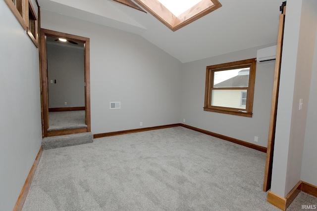 unfurnished bedroom featuring vaulted ceiling with skylight, visible vents, baseboards, a wall unit AC, and carpet floors