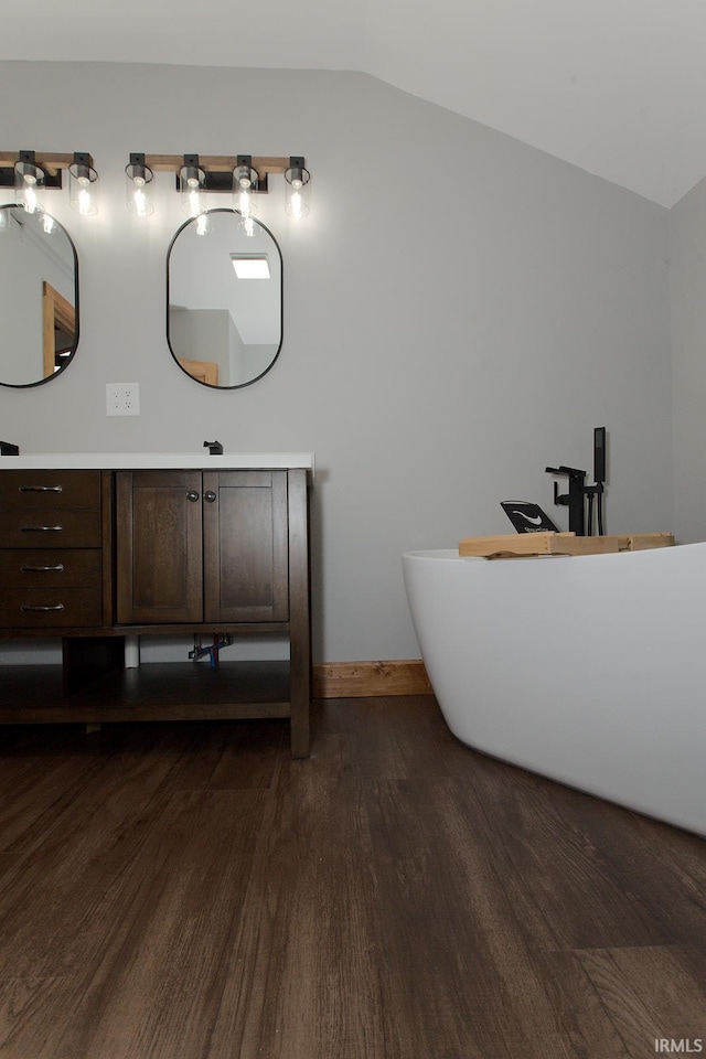 bathroom featuring lofted ceiling, wood finished floors, vanity, baseboards, and a freestanding bath