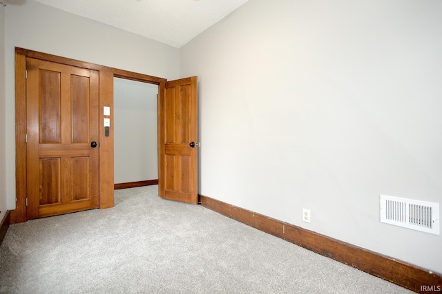 spare room featuring light carpet, lofted ceiling, visible vents, and baseboards