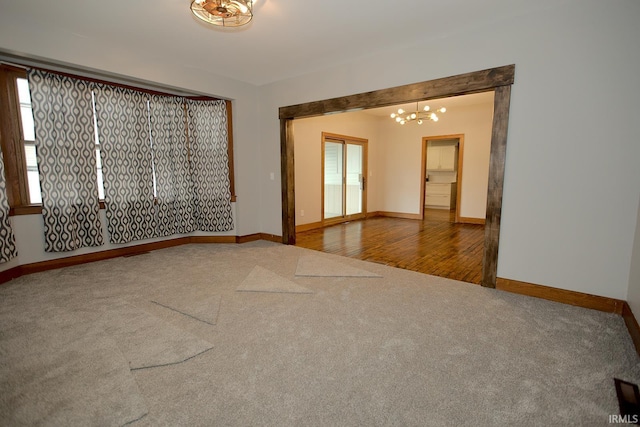 carpeted spare room featuring baseboards, an inviting chandelier, and a healthy amount of sunlight