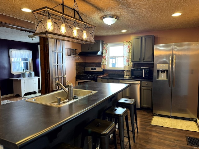 kitchen featuring stainless steel appliances, a sink, visible vents, dark countertops, and dark wood finished floors