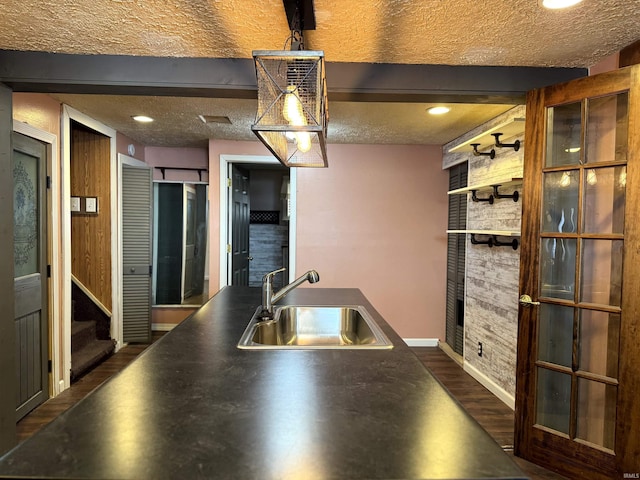 kitchen featuring dark wood-type flooring, a sink, a textured ceiling, and beamed ceiling