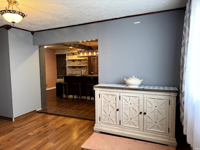 corridor featuring crown molding, a textured ceiling, baseboards, and wood finished floors