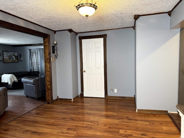 interior space with a textured ceiling, ornamental molding, wood finished floors, and baseboards