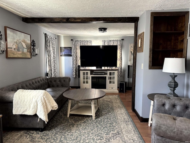 living room with a textured ceiling, a fireplace, wood finished floors, baseboards, and beamed ceiling