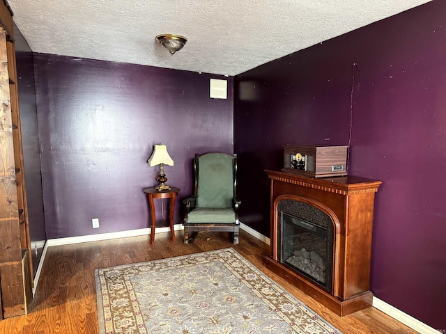 sitting room with a glass covered fireplace, baseboards, and wood finished floors