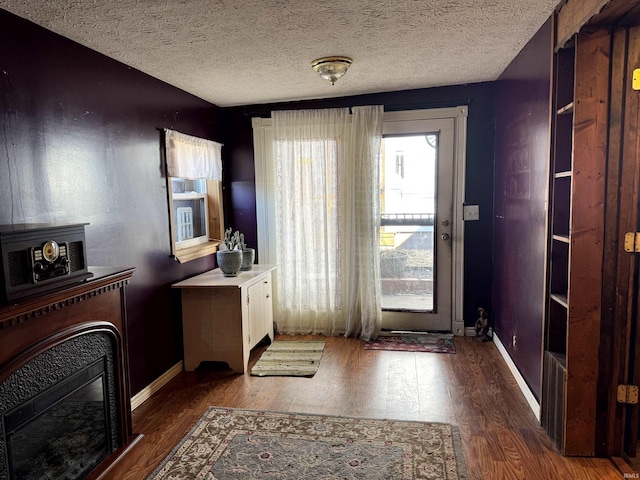 entryway featuring a fireplace, a textured ceiling, baseboards, and wood finished floors