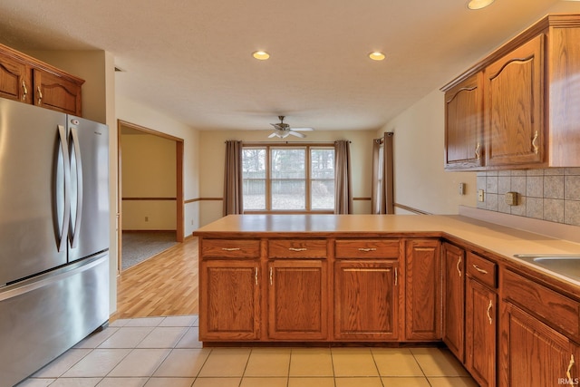 kitchen featuring freestanding refrigerator, brown cabinets, a peninsula, and light tile patterned floors