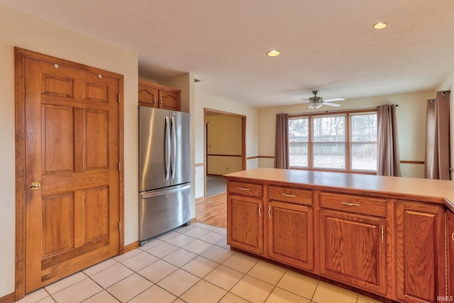 kitchen with light countertops, freestanding refrigerator, brown cabinets, and light tile patterned floors