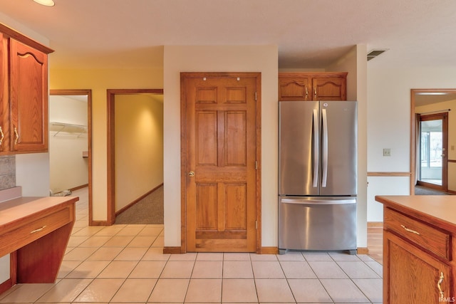 kitchen with light tile patterned floors, visible vents, brown cabinets, and freestanding refrigerator