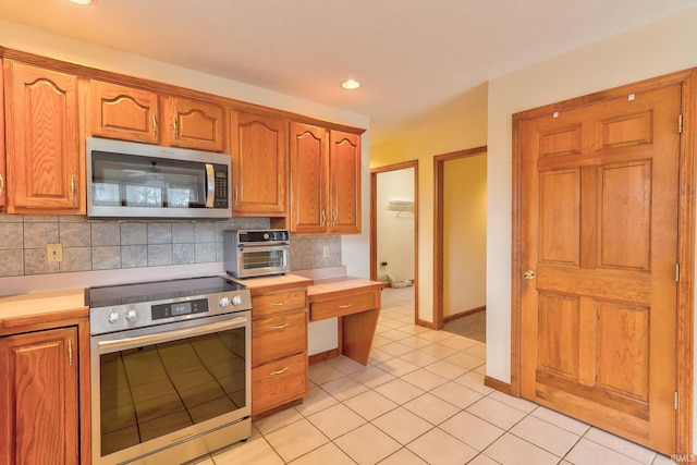 kitchen featuring light tile patterned floors, light countertops, backsplash, appliances with stainless steel finishes, and brown cabinetry