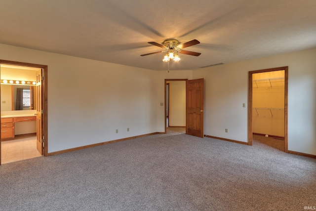 unfurnished bedroom featuring light carpet, ensuite bathroom, a walk in closet, and baseboards