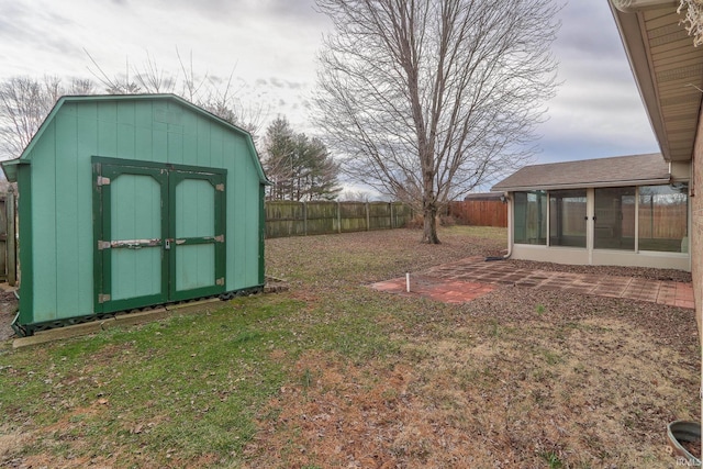 view of yard with a sunroom, a fenced backyard, a storage shed, and an outbuilding