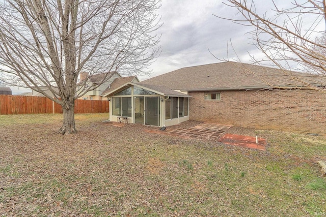 rear view of house with a sunroom, roof with shingles, fence, a yard, and brick siding