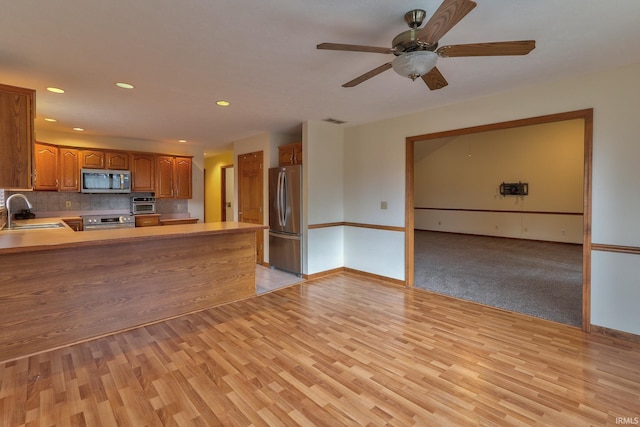 kitchen featuring stainless steel appliances, a sink, light wood-style floors, backsplash, and brown cabinetry