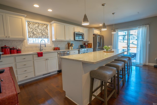 kitchen with a kitchen island, a sink, white cabinets, appliances with stainless steel finishes, and dark wood-style floors