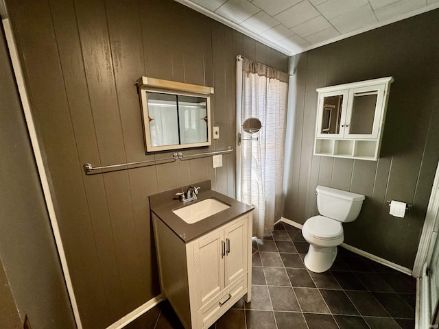 bathroom featuring wooden walls, baseboards, toilet, tile patterned flooring, and vanity