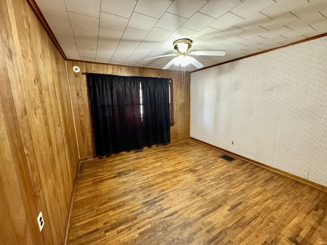 unfurnished room with baseboards, visible vents, ceiling fan, ornamental molding, and wood finished floors