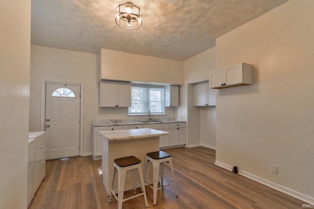 kitchen featuring a center island, a breakfast bar area, dark wood-type flooring, a sink, and baseboards