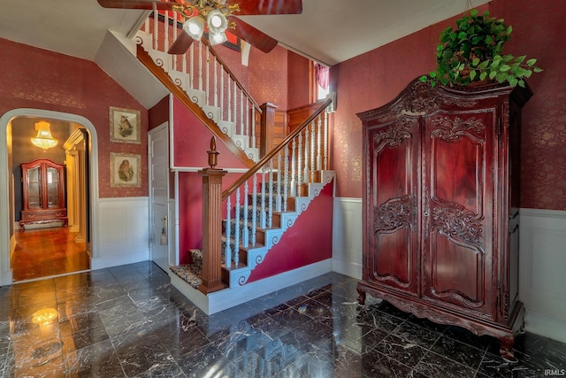 staircase featuring marble finish floor, arched walkways, and wainscoting