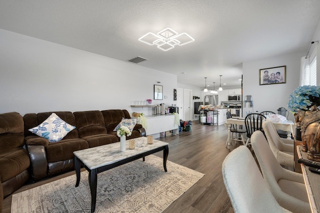 living area with visible vents, dark wood finished floors, a textured ceiling, and an inviting chandelier