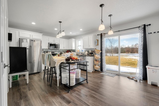 kitchen with hanging light fixtures, appliances with stainless steel finishes, dark wood-style flooring, and white cabinets