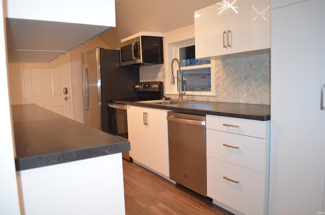 kitchen with appliances with stainless steel finishes, dark countertops, wood finished floors, and white cabinetry